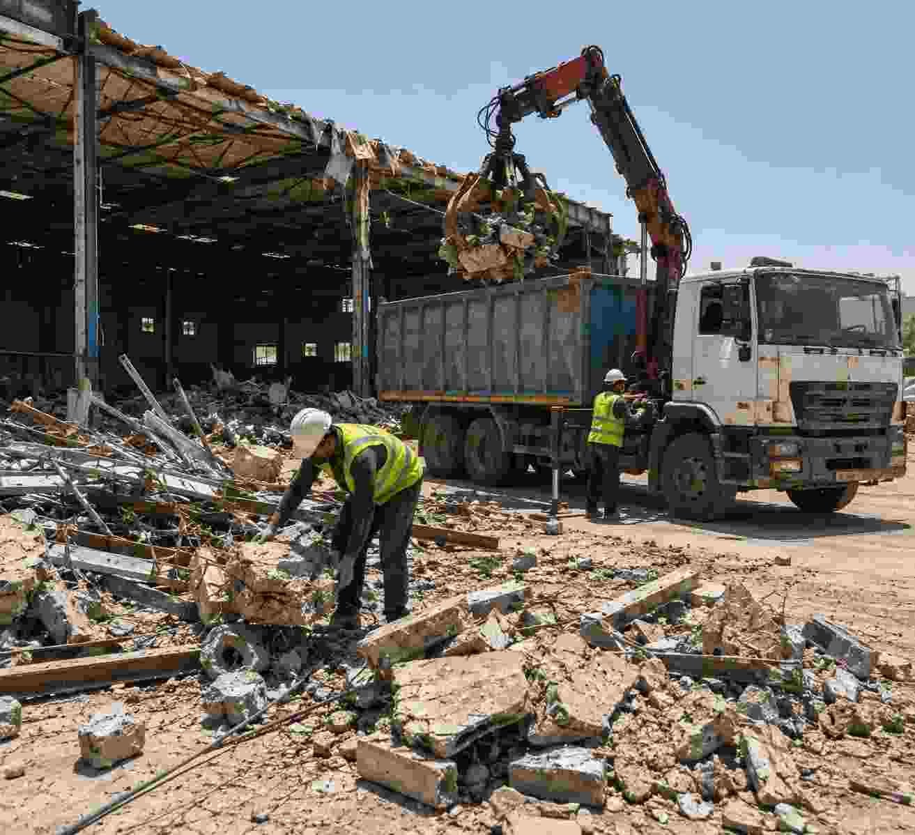 Workers clearing concrete and steel debris after partial warehouse demolition in Dubai